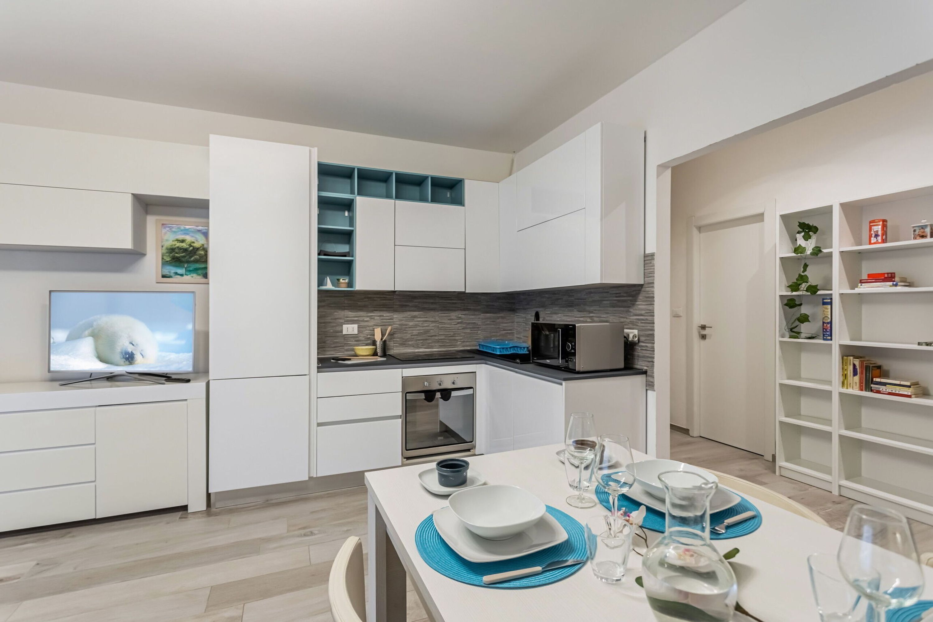 Una cocina moderna con armarios blancos, microondas integrado y un comedor con mesa dispuesta para dos.