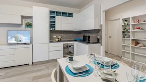 Una cocina moderna con armarios blancos, microondas integrado y un comedor con mesa dispuesta para dos.