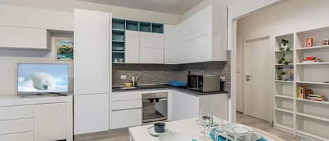 Una cocina moderna con armarios blancos, microondas integrado y un comedor con mesa dispuesta para dos.
