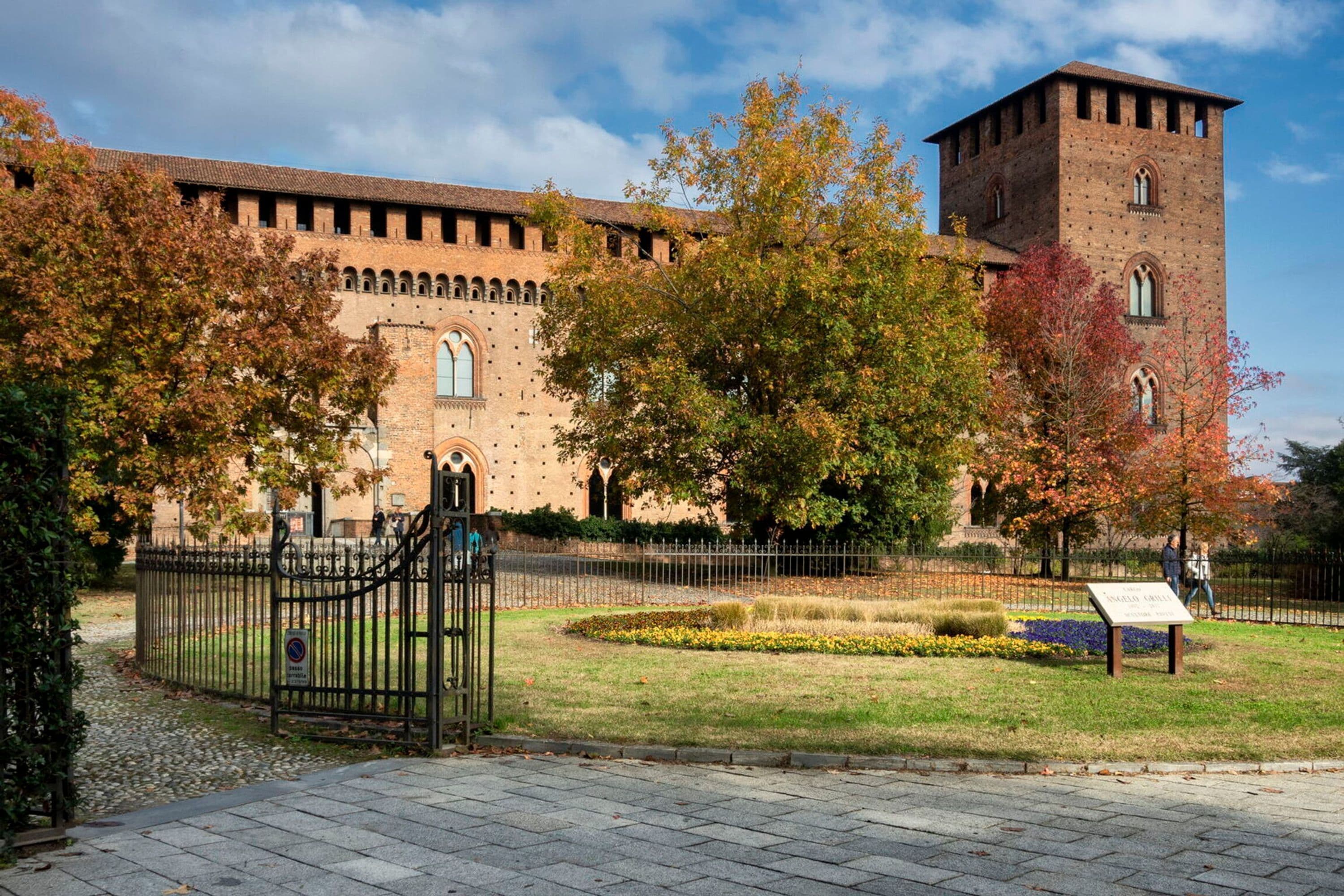 A historic building with a prominent tower, surrounded by a well-maintained garden and a metal fence.
