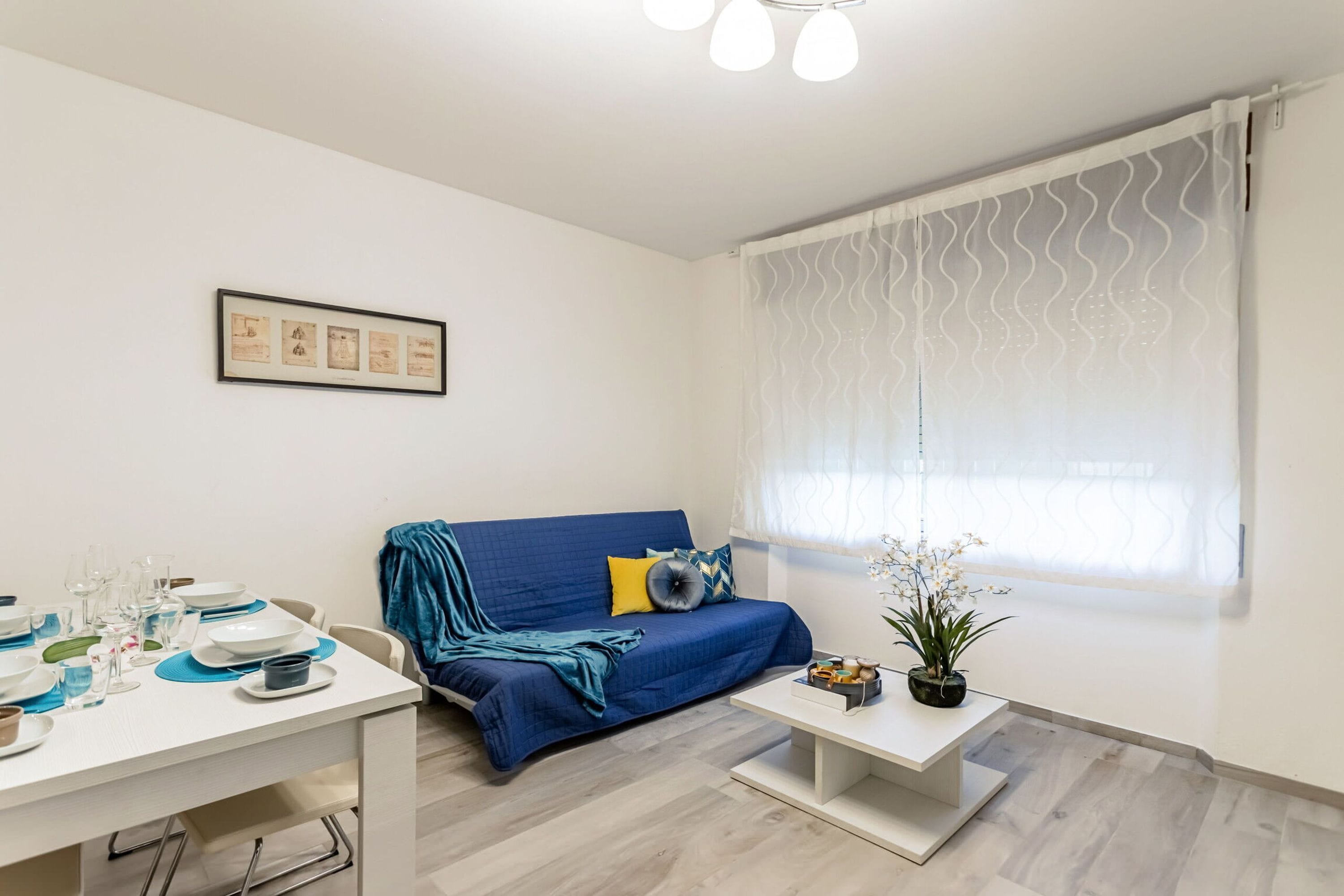Una sala moderna con un sofá, una mesa de comedor y una ventana con cortinas traslúcidas.