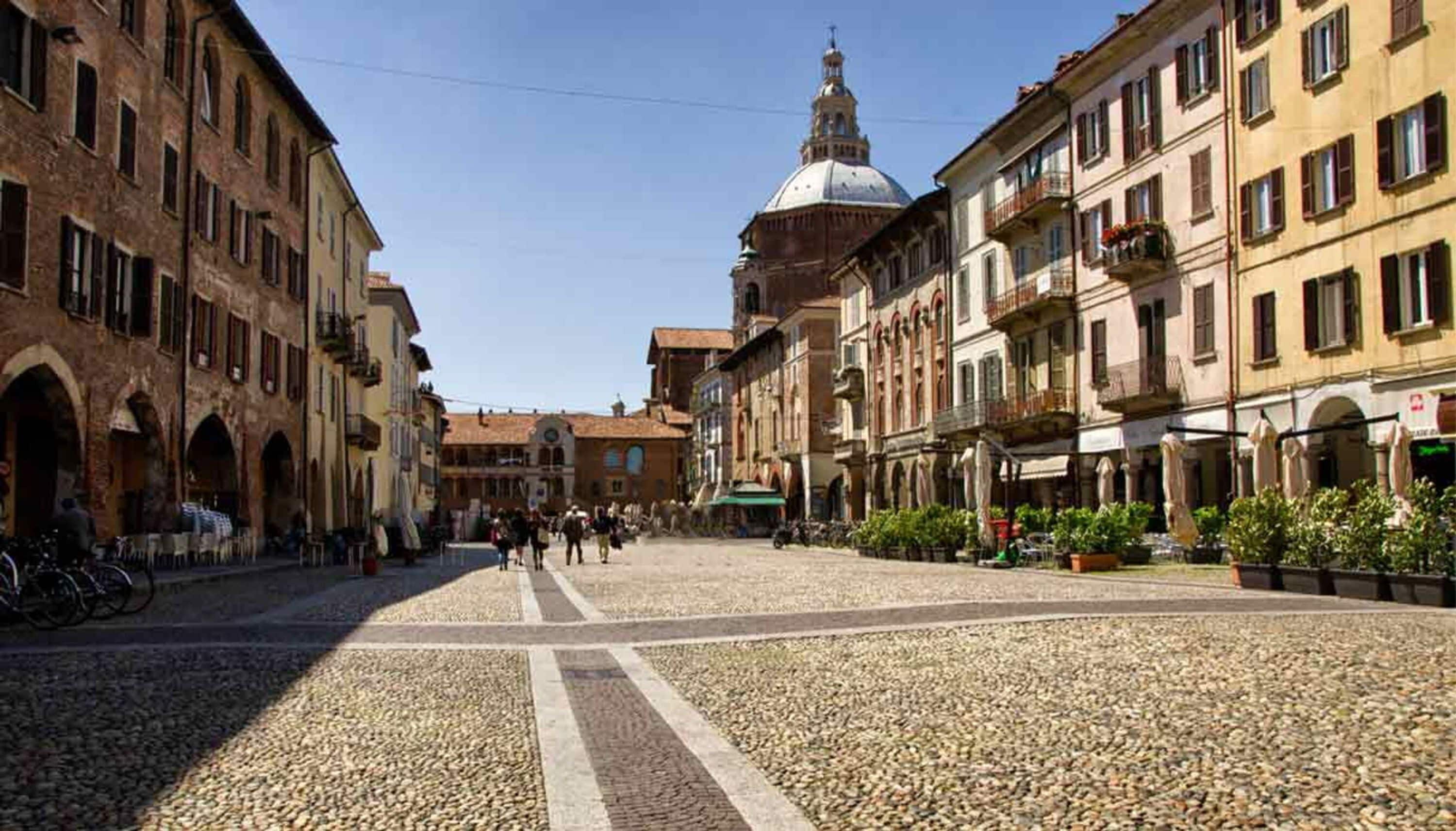 Una plaza adoquinada con edificios históricos, una estructura en forma de cúpula y zonas de estar al aire libre.