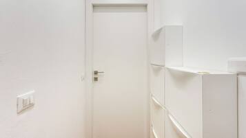 Une porte blanche fermée, dotée d’une poignée et d’un trou de serrure, un interrupteur blanc sur le mur et un meuble blanc avec des tiroirs.