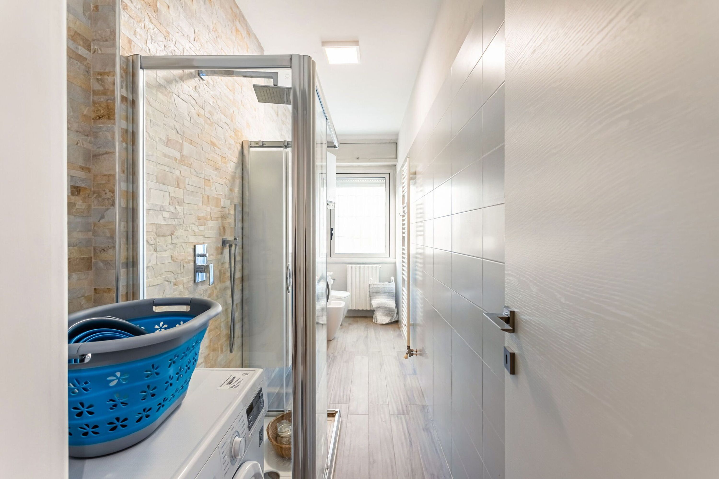 Un couloir étroit avec un panier à linge, un espace douche et une vue sur une salle de bain.