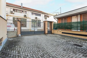 Un patio con suelo empedrado, una entrada porticada y un edificio con varias ventanas y unidades de aire acondicionado.
