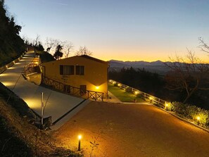 Un edificio con techo inclinado, un camino pavimentado que conduce a él y vistas de montañas distantes.