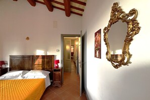 Un dormitorio con una cama de madera, una mesita de noche, una lámpara roja y un espejo grande y ornamentado en la pared.