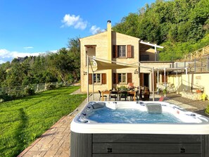 Un jacuzzi en un patio trasero con terraza, zona de comedor y una casa con balcón.