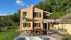 Una casa de dos pisos con un patio, un jacuzzi y vistas del entorno cubierto de vegetación.
