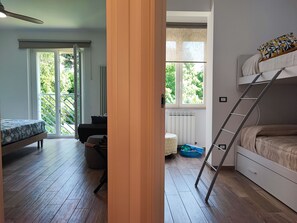 Ein Zimmer mit einem Etagenbett, einem Schreibtisch, einem Stuhl, einem Heizkörper und einem Fenster mit Blick auf Grünflächen.