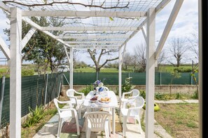 Eine Außenpatio mit einer weißen Pergola, einem Esstisch und Stühlen.