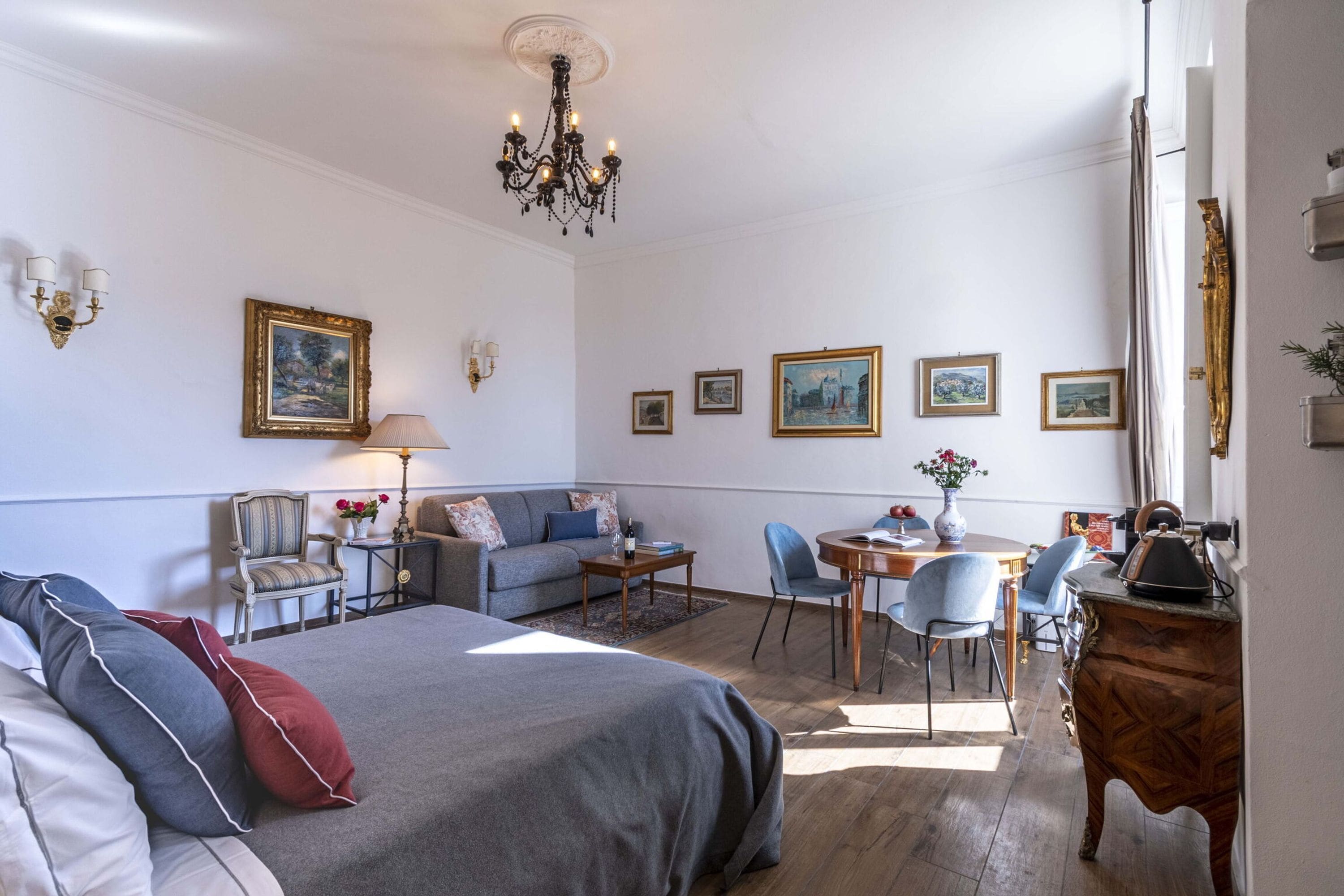 Ein Hotelzimmer mit Bett, einer Couch, einem Esstisch mit Stühlen, einer Chandelierleuchtre und Wandbildern.