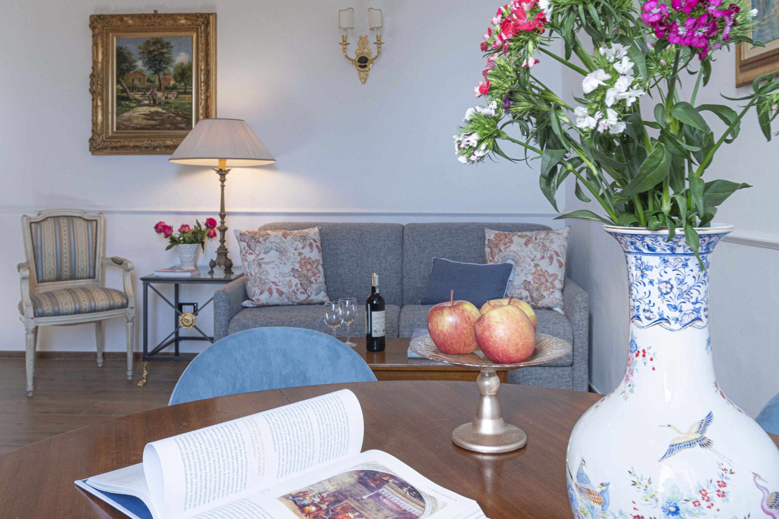 Ein Zimmer mit Esstisch, einer Couch, einem Sessel, einer Blumenvase, einer Lampe und einem gerahmten Bild an der Wand.