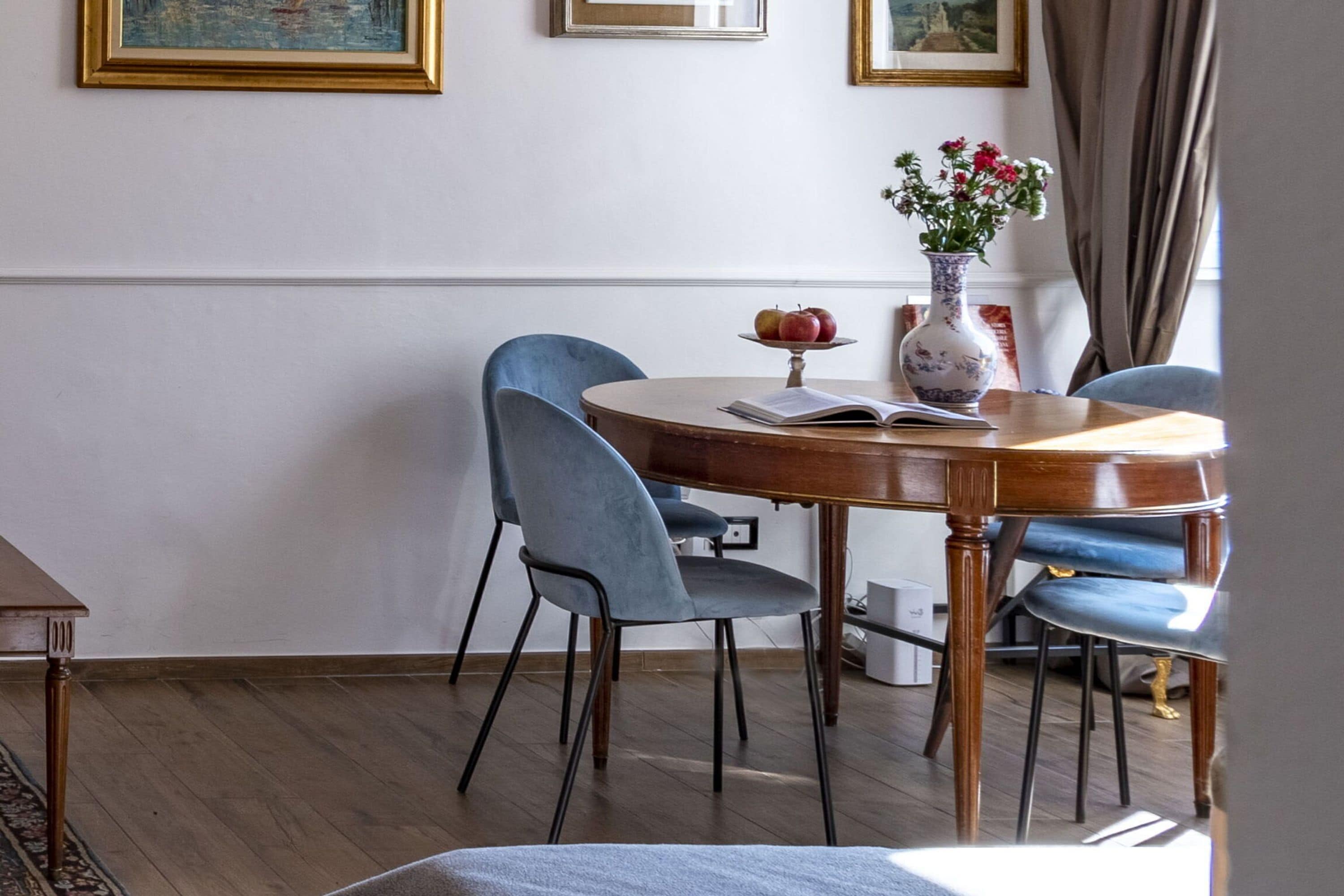 Ein Essbereich mit einem runden Tisch, blauen Stühlen, einer Blumenvase und einem Buch.