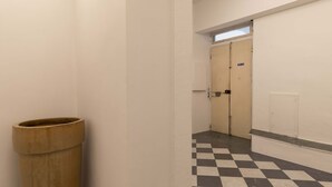 Um corredor estreito com piso xadrez, uma lixeira e uma porta com um aviso.