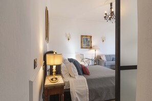 Quarto de hotel com cama, mesa de cabeceira com abajur, poltrona, sofá e um quadro na parede.
