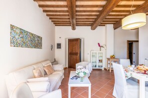 A living room with a sofa, a dining table with chairs, a wooden ceiling, and a painting on the wall. - Serafini Holiday Home (Colli al Metauro)