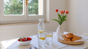 Een tafel met een schaal aardbeien, een waterkan, glazen met citroenpartjes, een vaas tulpen en een mand croissants.