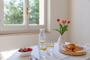 A table with a bowl of strawberries, a pitcher of water, glasses with lemon slices, a vase with tulips, and a basket of croissants. - Casale Oleandro Marino - Nocciola Apartment (Porto Recanati)