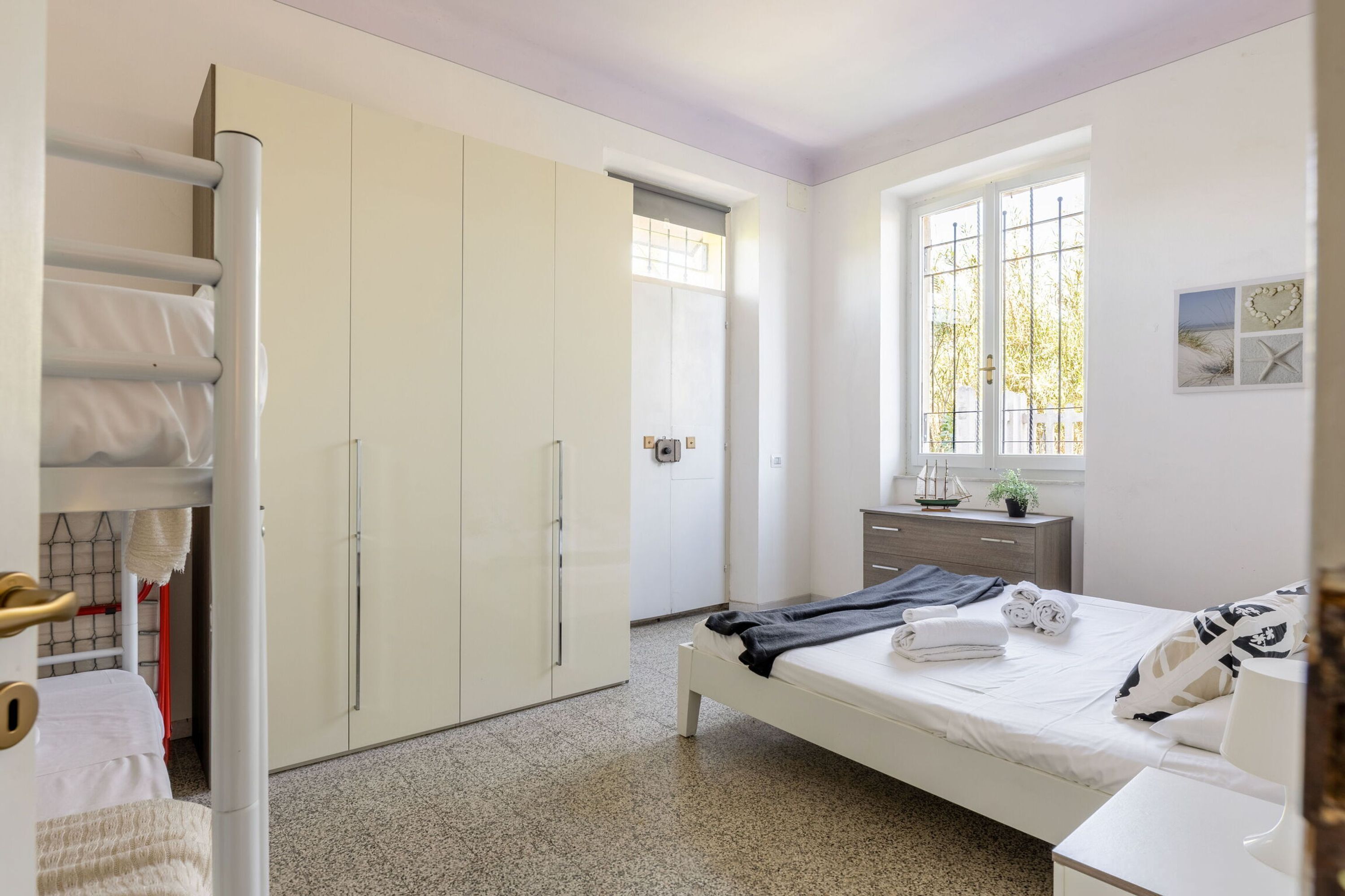 A bedroom with a bed, a dresser, a window with a view, and a wardrobe.