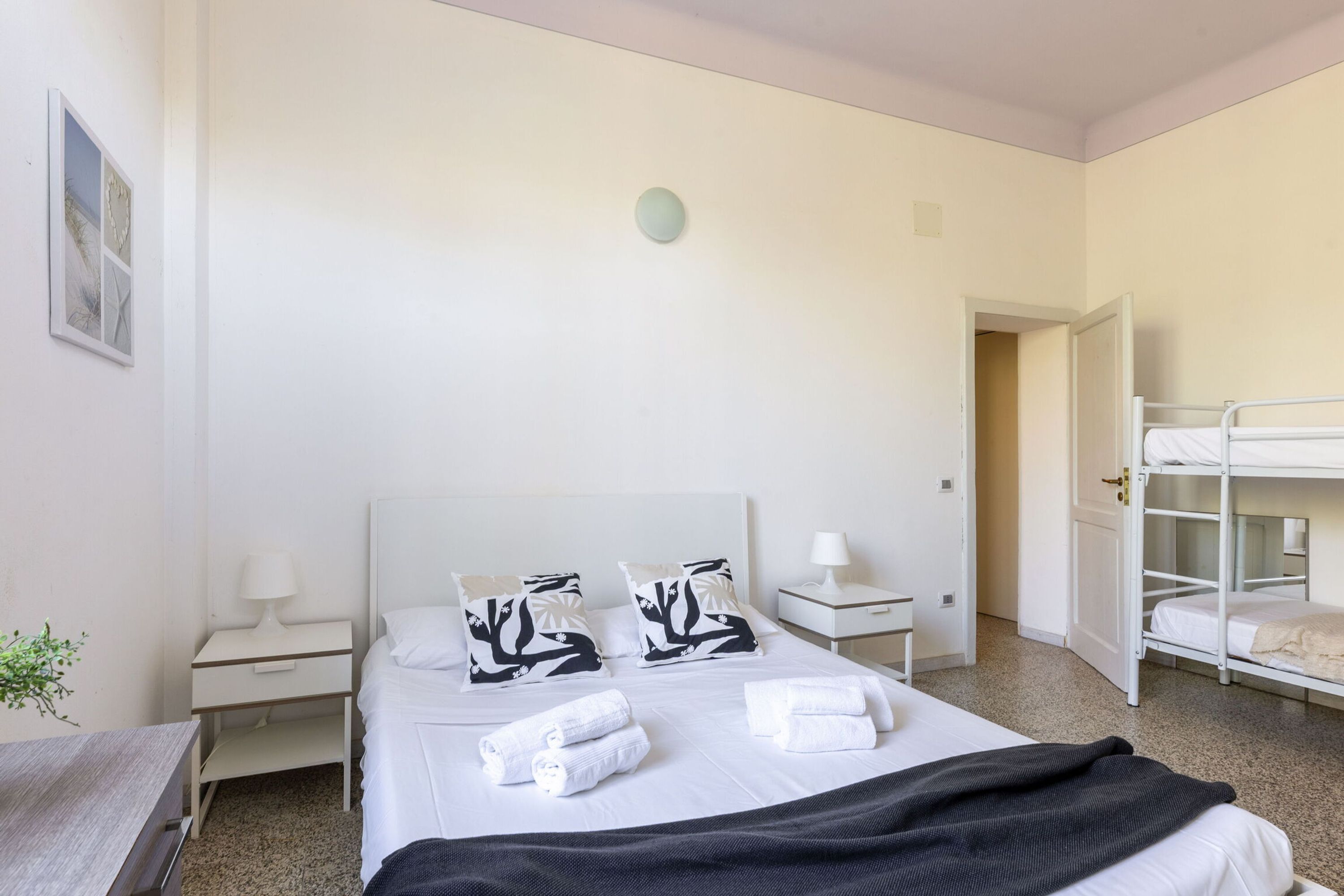 A hotel room with a single bed, two bedside tables, a nightstand, a window, and a bunk bed in the corner.