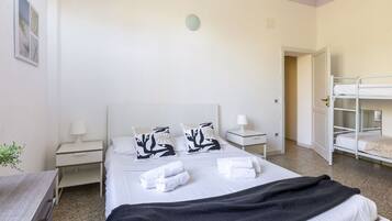 A hotel room with a single bed, two bedside tables, a nightstand, a window, and a bunk bed in the corner.
