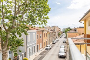 Straßenansicht mit Gebäuden, parkenden Autos und Bäumen.