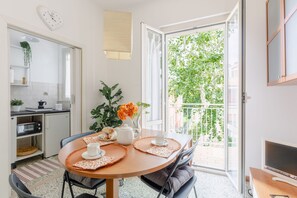 Eine moderne Küche mit Mikrowelle, Toaster und Kaffeemaschine. Ein Esstisch mit Stühlen, ein Fernseher und ein Balkon mit Blick auf Bäume.