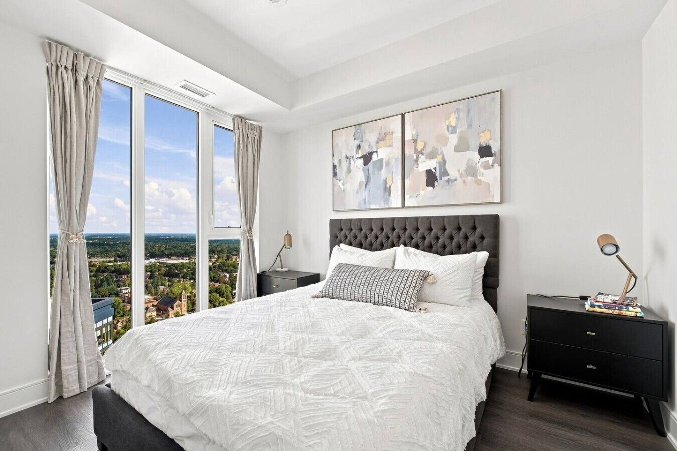 A bedroom with a large bed, a view of the city, and abstract art on the wall.