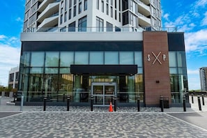 A modern building with a glass facade, a prominent 'SXP' sign, and a patterned pavement. - Sleek 2BR Condo | City View | Pool, Gym & Bowling (Kitchener)