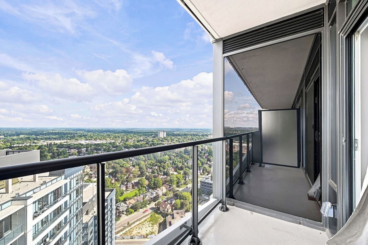 A balcony with a clear view of a cityscape, including buildings and greenery.