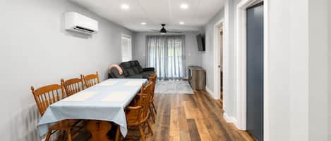 A dining area with a table set for four, wooden chairs, a ceiling fan, and a TV mounted on the wall.