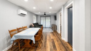 A dining area with a table set for four, wooden chairs, a ceiling fan, and a TV mounted on the wall.