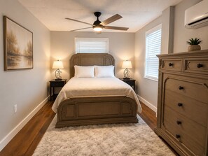 A bedroom with a bed, a ceiling fan, bedside lamps, a dresser, and a painting on the wall.