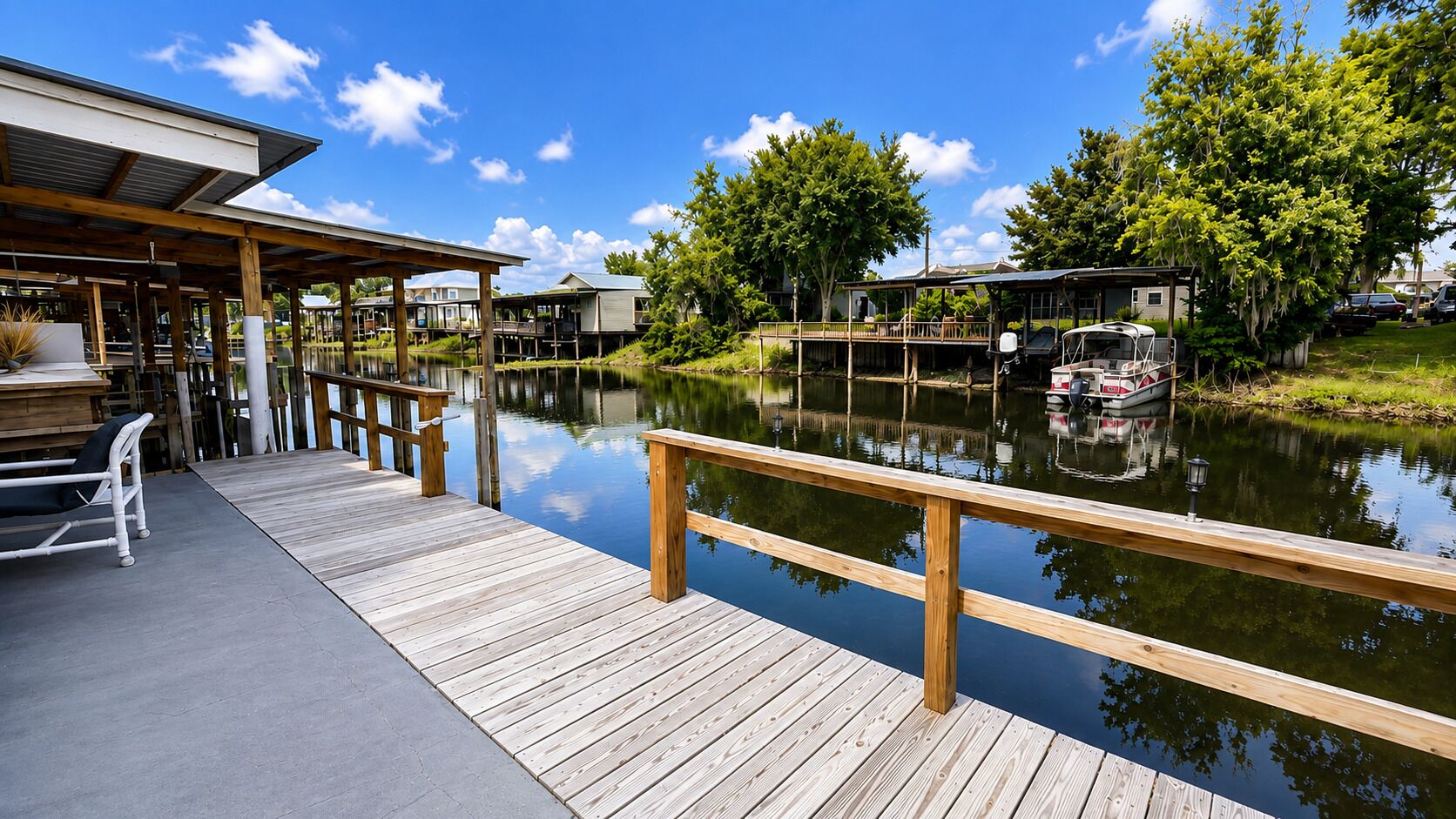 A wooden dock extending over calm water, with a covered seating area and a boat docked on the right.