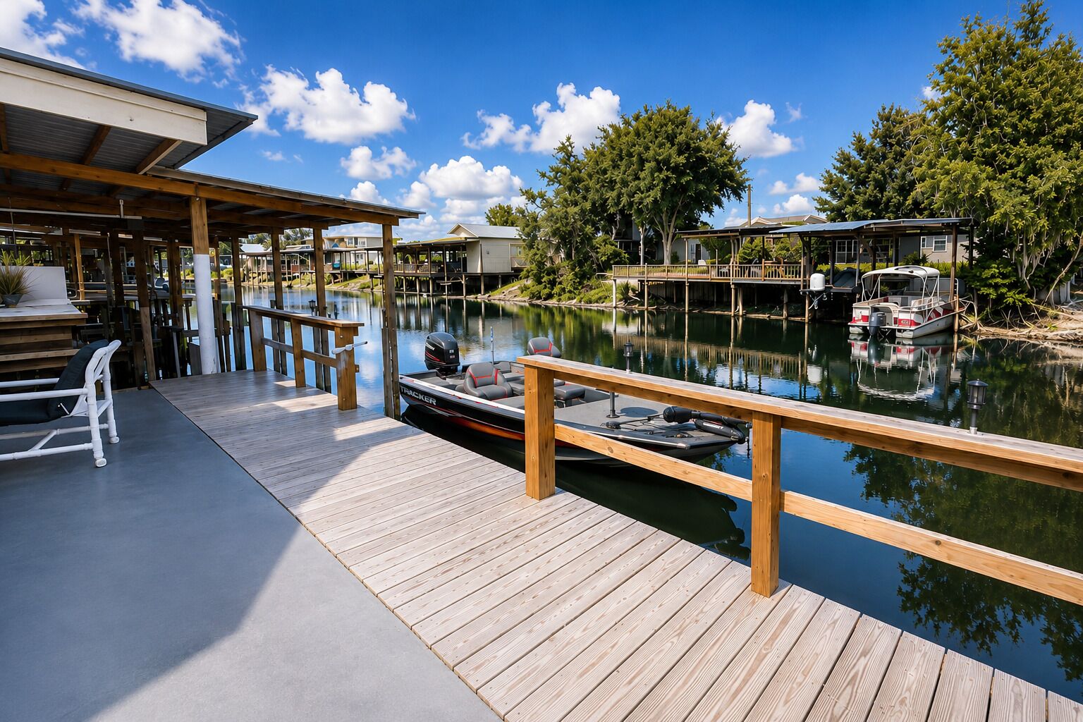 A wooden dock extending over calm water with a boat docked, surrounded by trees and buildings.