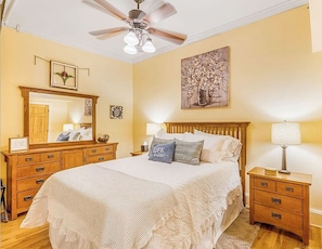 A bedroom with a bed, nightstands, a dresser, a ceiling fan, and a wall-mounted painting. - The Asheville Jewel Downtown Asheville 1BR with queen bed, full kitchen, Wi-Fi, and elevator. (Asheville)