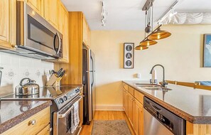 A kitchen with wooden cabinets, stainless steel appliances, a microwave, a stove, and a dishwasher. - The Asheville Jewel Downtown Asheville 1BR with queen bed, full kitchen, Wi-Fi, and elevator. (Asheville)