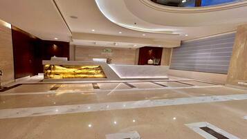 Eine moderne Lobby mit einer Rezeption, einer großen Wanddekoration und einer hohen Decke mit eingelassener Beleuchtung.