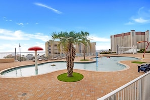 A pool area with a palm tree, lounge chairs, and a view of high-rise buildings. - Laketown Wharf 824 | Beach View (Panama City Beach)