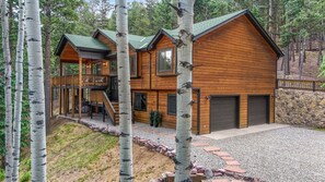 A log cabin with a deck, multiple windows, and a stone wall. - Private Mountain Retreat w/Hot Tub & Game Room I Sleeps 12 (Woodland Park)