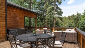 Een houten terras met een ronde tafel en stoelen, omringd door rieten meubels, met uitzicht op een bebost gebied.