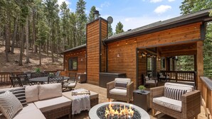 Une terrasse en bois avec des meubles d’extérieur, un foyer et une vue sur une zone boisée.