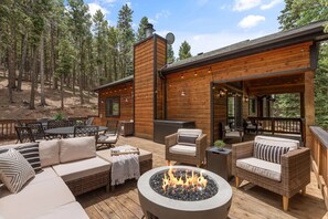 A wooden deck with outdoor furniture, a fire pit, and a view of a forested area. - Private Mountain Retreat w/Hot Tub & Game Room I Sleeps 12 (Woodland Park)