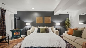 Une chambre à coucher avec un lit, deux lampes de chevet, un mur foncé orné de deux œuvres d’art encadrées, un plancher en bois et une cheminée.