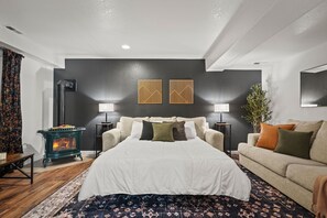 A bedroom with a bed, two bedside lamps, a dark wall with two framed artworks, a wooden floor, and a fireplace. - Private Mountain Retreat w/Hot Tub & Game Room I Sleeps 12 (Woodland Park)