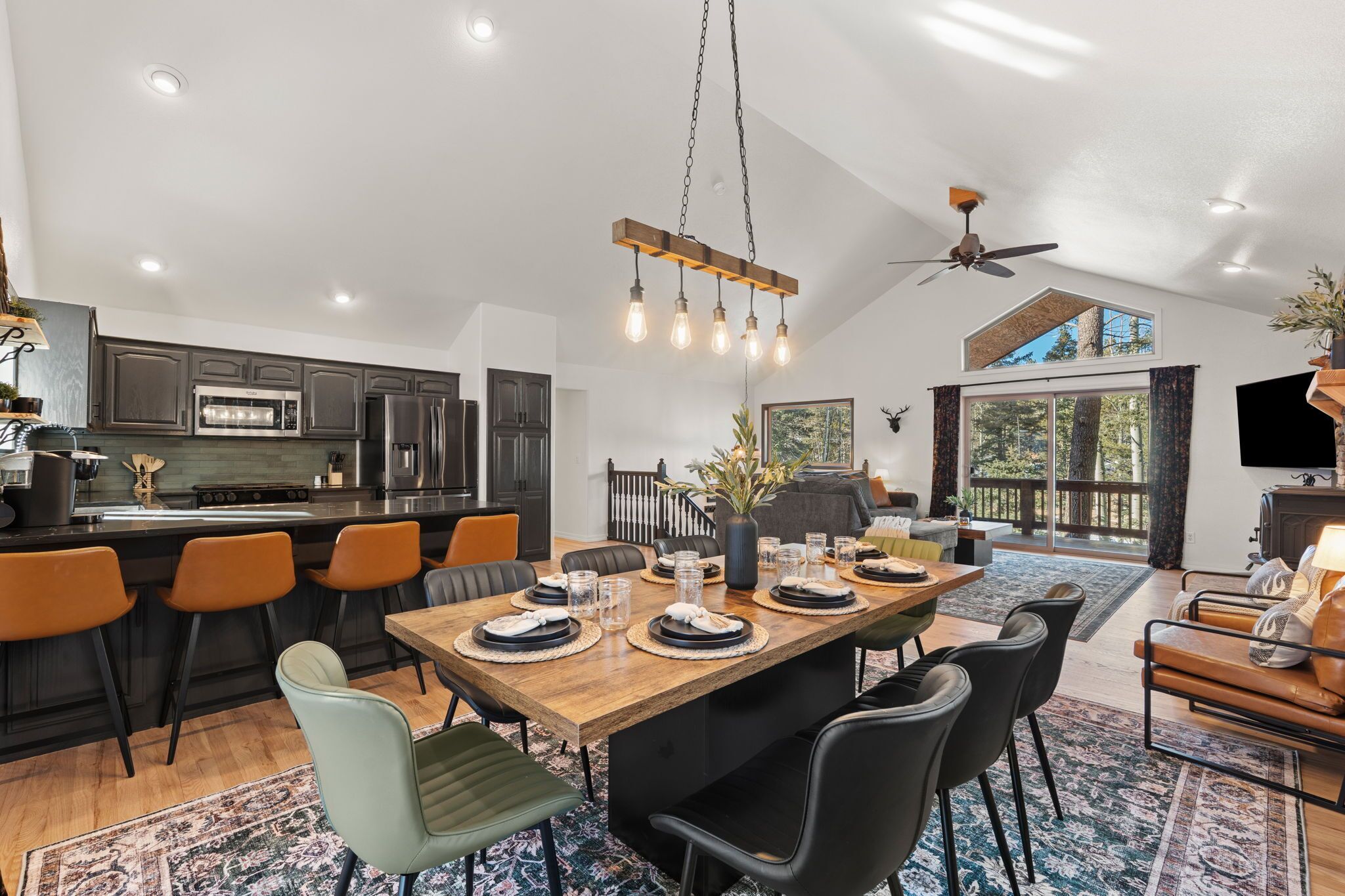 A spacious kitchen with modern appliances, a dining area with a wooden table and chairs, and a large window offering a view of the outdoors.