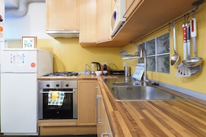 A compact kitchen with wooden cabinets, a gas stove, a built-in oven, a sink, and various kitchen utensils hanging on the wall. - Suite Meda in Milano (Milan)