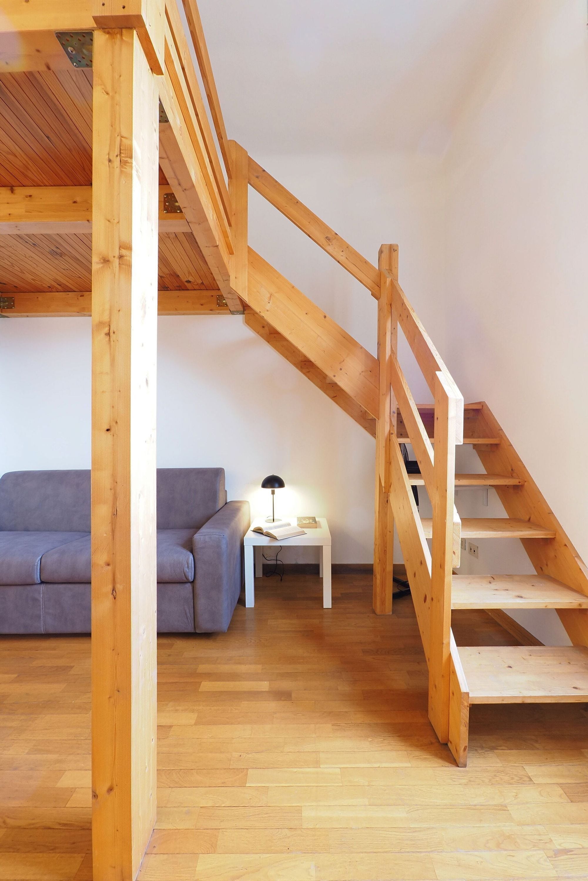 A loft-style room with a wooden staircase, a sofa, and a small table with a lamp.