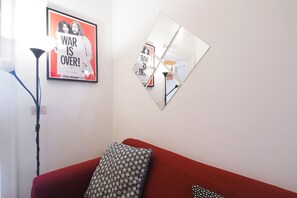 A room with a red sofa, a framed poster, a floor lamp, and a wall-mounted mirror. - Suite Meda in Milano (Milan)